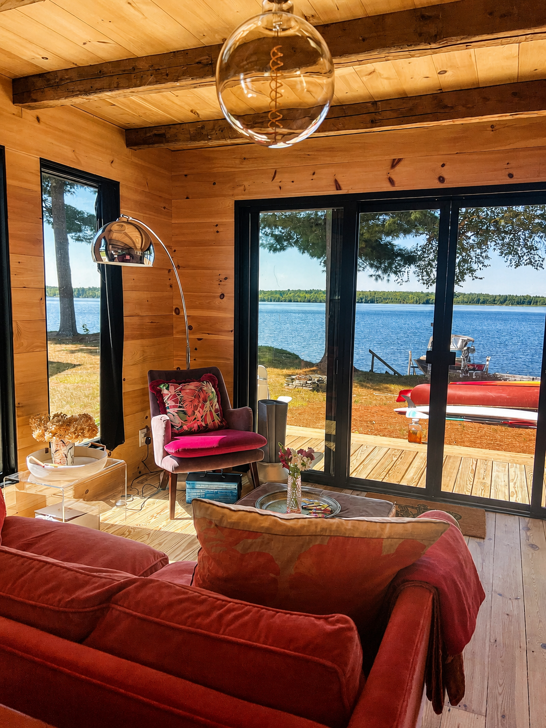 Warm pine-panelled living room with a red sofa framing wide sliding doors onto the lake